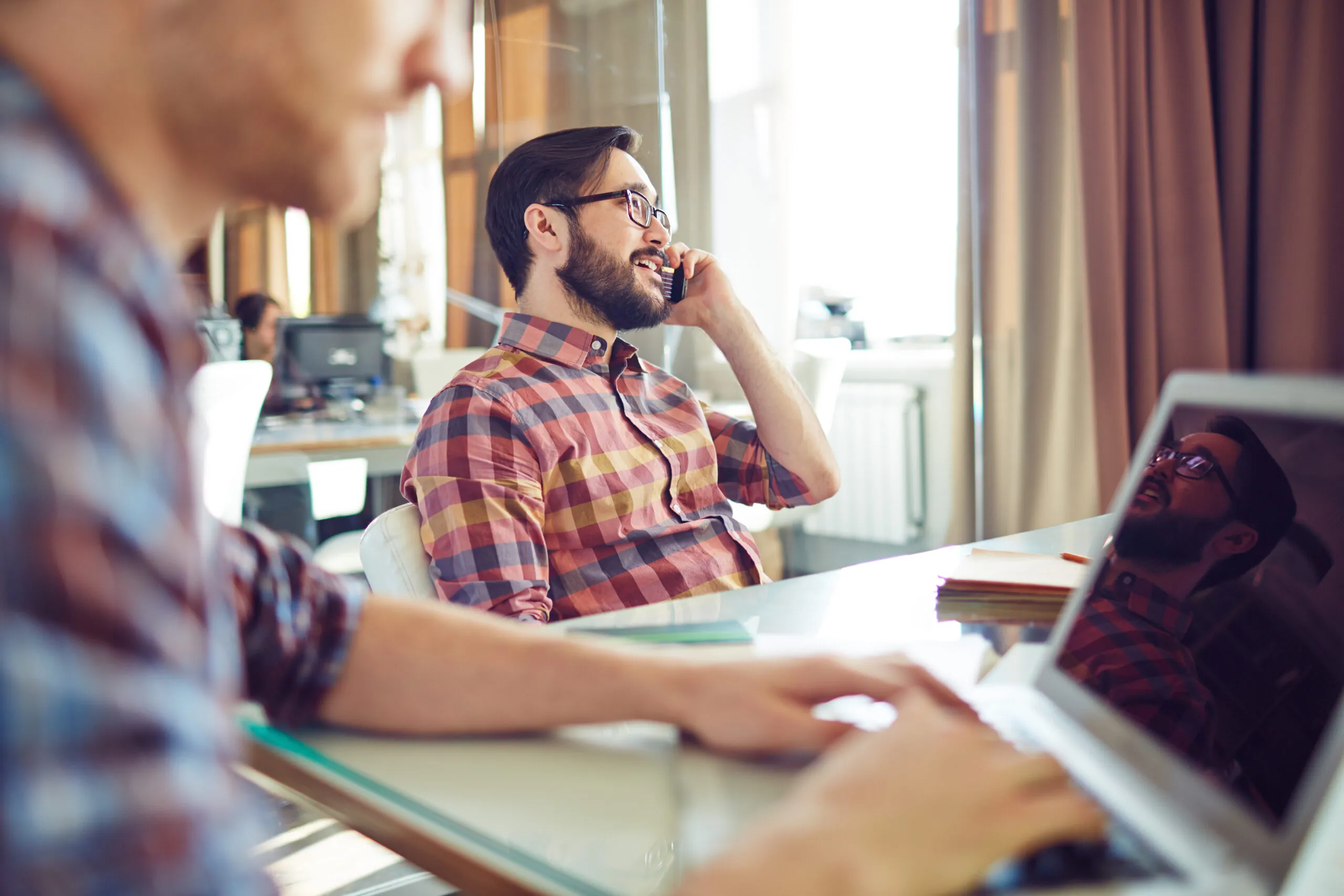 Young,Businessman,Sitting,By,Workplace,And,Speaking,On,The,Phone